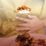 Woman eating spicy food while holding her stomach.